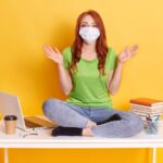 woman-medical-mask-young-girl-dressed-green-t-shirt-jeans-sitting-table-with-crossed-legs_176532-11470