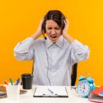 annoyed-young-call-center-girl-wearing-headset-sitting-desk-holding-her-head-with-closed-eyes-isolated-orange_141793-76437