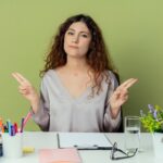 impressed-young-pretty-female-office-worker-sitting-desk-with-office-tools-pointings-sides-isolated-olive-background_141793-63160