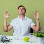 with-closed-eyes-young-handsome-male-student-sitting-desk-with-school-tools-showing-meditation-gesture-isolated-olive-green_141793-83905