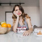 bored-young-lady-sitting-table-with-cake-fruits-pretty-white-girl-posing-breakfast_197531-9715