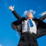 excited-businessman-raising-his-arms-against-sky_23-2147956326