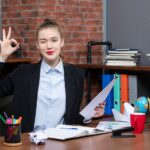 top-view-confident-young-lady-sitting-table-holding-document-making-eyeglasses-gesture-office_140725-106183